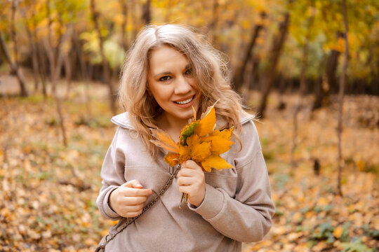Joyful woman holding autumn leaves in park &mdash; deep nature appreciation. Personal harmony and seasonal changes acceptance. Attractive person collecting yellow foliage expressing positive emotions.