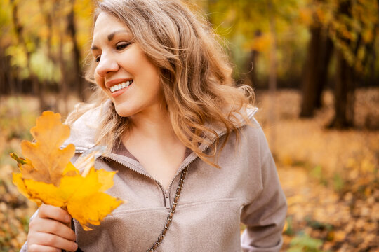 Relaxed woman admiring autumn leaves in forest &mdash; enjoying simple things. Emotional restoration and stress management. Smiling lady looking at yellow foliage feeling calm during relaxing walk.
