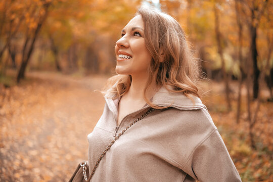 Happy woman tourist in autumn forest. Joyful smiling traveler stands among yellow trees looking up. Modern blogger enjoying mental health relaxation outdoors.