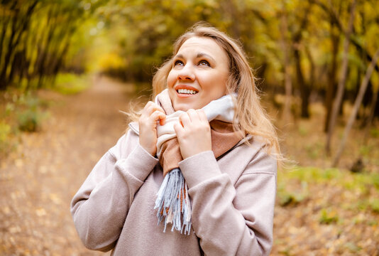 Happy woman tourist in plaid scarf in autumn forest. Joyful smiling traveler enjoying warm weather among yellow trees. Concept of cozy autumn fashion outdoors.