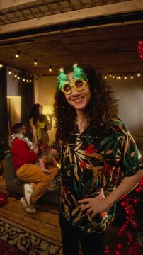 Vertical portrait of young Caucasian man wearing novelty Christmas glasses, toasting with champagne glass at festive party. Footage suitable for holiday social media marketing