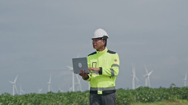 Engineer Using Laptop in Wind Turbine Field Construction Safety Helmet Reflective Vest Renewable Energy Inspection Green Landscape Cloudy Sky Sustainable Technology Infrastructure