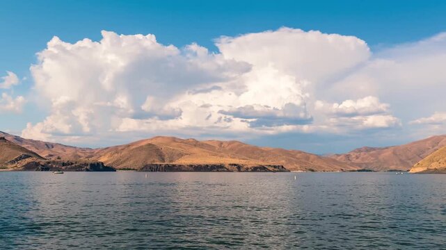 View of Lucky Peak Lake with rolling hills and fluffy white clouds under a bright blue sky in Ada County, Idaho, United States.