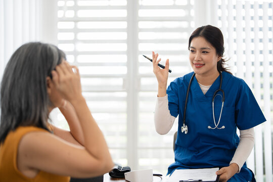 Female Doctor holding clipboard and listening to senior patient describing symptoms during home visit.