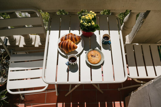 Sunny Balcony Breakfast Table with Croissants, Coffee Cups, Chocolate Cookie and Yellow Flowers . Summer coffee at sunny terrace.