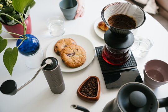 Pour Over Coffee Brewing with Cookies and Hand Grinder on white table. Professional coffee preparation. sunny day