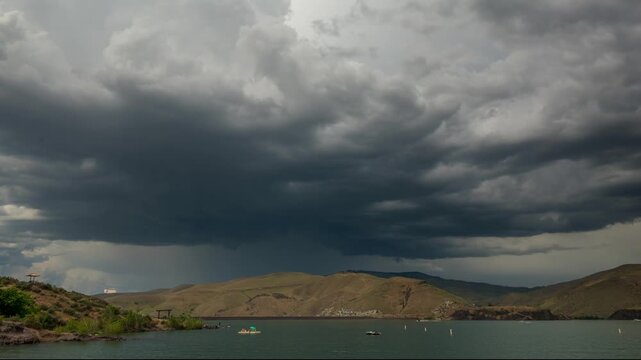 View of Lucky Peak Lake under dark storm clouds over rolling hills in Ada County, Idaho, United States.