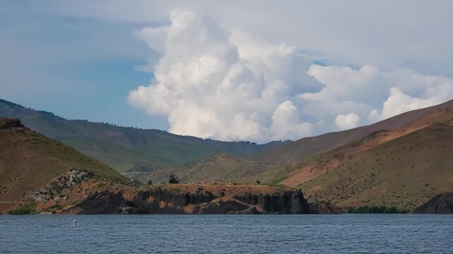 View of Lucky Peak Lake surrounded by rolling hills and rocky terrain under a large cumulus cloud in Ada County, Idaho, United States.