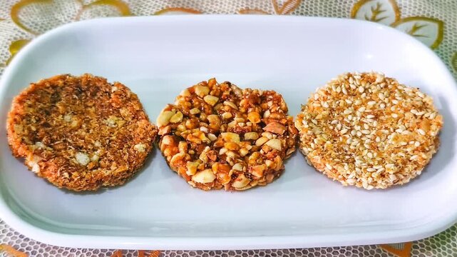 Traditional Indonesian enting enting crispy peanut sesame brittle snack cookies served neatly on a white ceramic platter over floral tablecloth top view ideal for Asian culinary dessert concept