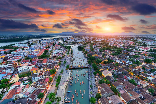 Boats float on the Thu Bon River in Hoi An Vietnam during bright sunset. The sky shows colors as the day ends