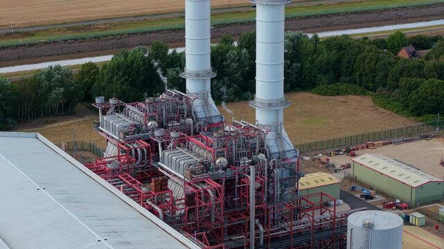 Close-up aerial view of intricate steam piping networks, HRSG ductwork, and exhaust stack base at Sutton Bridge power plant in Lincolnshire, UK