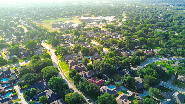 Paved residential roads weave through established subdivisions in prominent Dallas suburbs. Lush foliage frames single family roofs across welcoming neighborhoods of Coppell, Texas