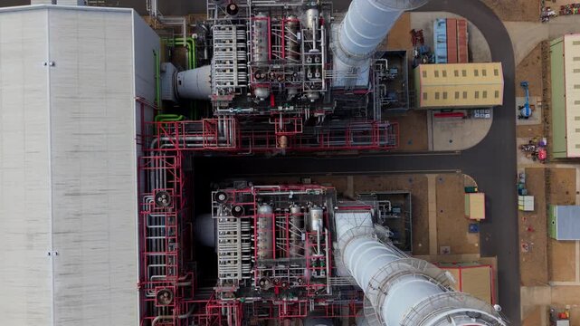 Close-up aerial view of intricate steam piping networks, HRSG ductwork, and exhaust stack base at Sutton Bridge power plant in Lincolnshire, UK