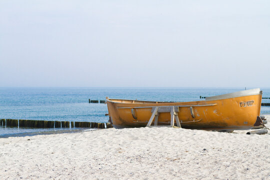 Gelbes Holzboot am hellen Sandstrand an der Ostsee vor ruhigem blauem Meer und klarem Himmel