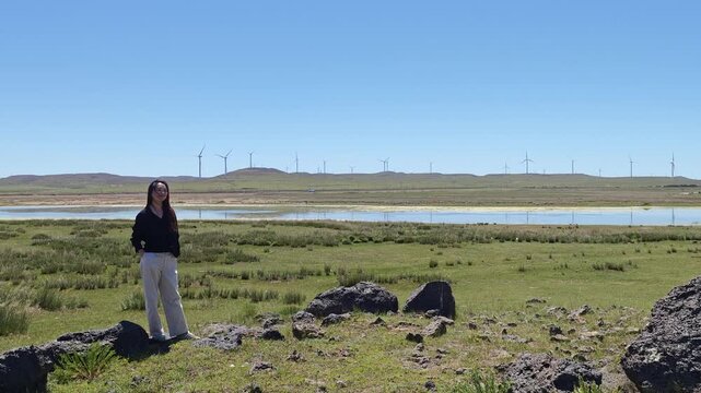 One Asian woman enjoying scenic landscape of salt lake wetland and distant wind turbines in summer in Ulan Hada Volcano Geopark, Ulanqab, Inner Mongolia, China