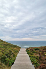 Fototapeta premium Serene Coastal Boardwalk Leading to the Ocean Under a Cloudy Sky for Relaxation and Travel Inspiration