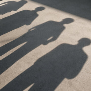 Photorealistic business concept showing overlapping shadows of several standing people cast across a plain floor, only the shadows visible and no actual people in frame. Visual metaphor for people.