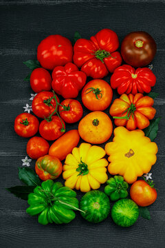 Assorted homegrown heirloom tomatoes with small flowers on a dark wooden background. Urban farming