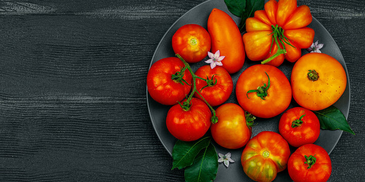 Assorted red and orange homegrown heirloom tomatoes with green leaves and small flowers