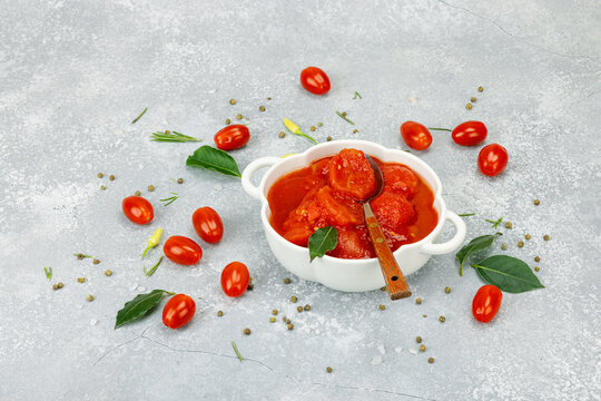 Canned whole peeled tomatoes in tomato juice in a white ceramic bowl with spoon. Rustic food styling