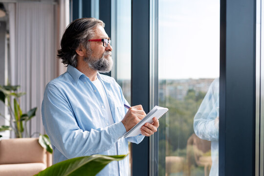 Mature man thinking and writing in modern office