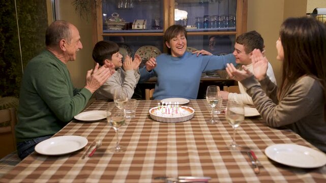 Family sings happy birthday to grandmother, clapping and kissing as she blows out candles on a lemon pie cake. Warm multigenerational celebration at home. Push-in shot, video 4K