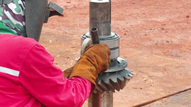 An industrial welder is performing precise metal grinding and machine part maintenance service at a factory workshop. Industrial working scene, close-up with selective focus.