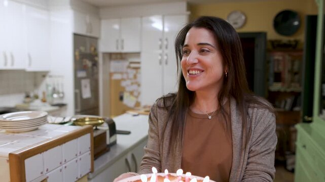 A mother carries a lemon pie cake with lit candles to her grandmother as family sings Happy Birthday. Grandchildren and grandfather join, toasting with wine. Tracking shot, video 4K