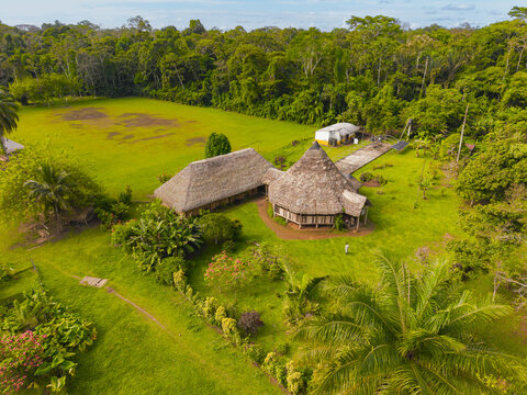 Aerial view of Lodge featuring traditional thatched-roof buildings set amidst a lush green lawn and dense Amazon rainforest in El Retiro, Sucumbios, Ecuador.
