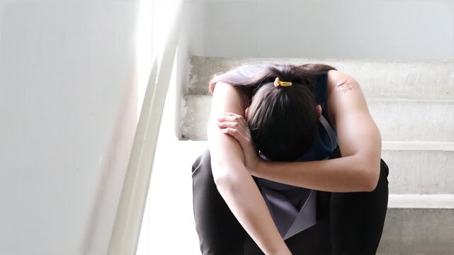 Low wage housekeeping maid in despair, head down and sighing on indoor stairwell, concept of sadness and struggling to earn money