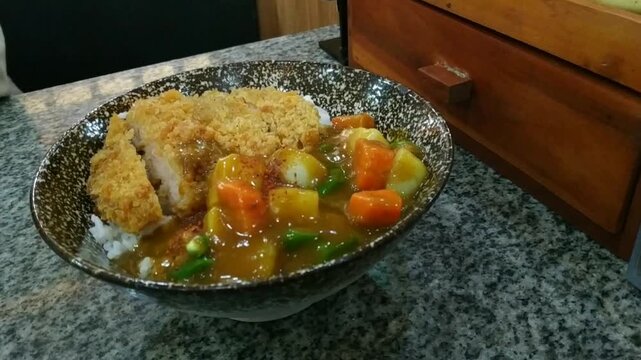 Close-up view of delicious Japanese katsu curry rice in a speckled ceramic bowl. Features a crispy breaded chicken cutlet served with rich brown curry sauce, chunky carrots, and potatoes over white ri