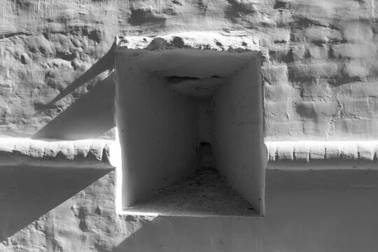 Old weathered white monastery fortification wall featuring a deep recessed embrasure creating dramatic sharp shadows in a minimalist monochrome architectural composition under bright daylight