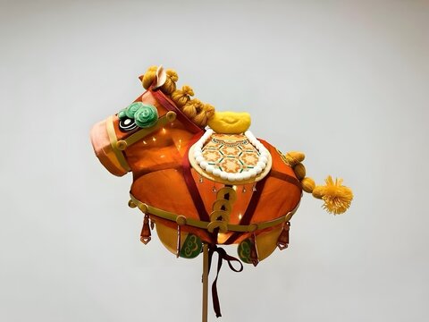Ornate traditional Chinese horse figurine displayed against a clean neutral backdrop, featuring vivid orange tones, embroidered saddle details, braided mane, tassels, and handcrafted decorative