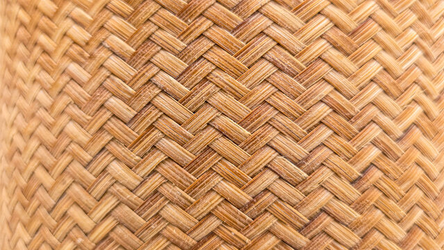 Close-up view of natural woven bamboo texture featuring an intricate diagonal basket weave pattern in warm golden brown tones. The detailed organic material creates a rustic, traditional, and handcraf