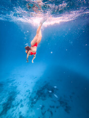 Female freediver descending through brilliant blue seawater with snorkeling fins, bubbles and rocky seabed below, conveying adventure, summer travel, freedom and ocean exploration. © JairoMZ