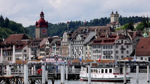 Lucerne, Switzerland - 21 August 2026: View of the historic waterfront in Lucerne with traditional buildings, the clock tower, and a boat docked on Lake Lucerne.