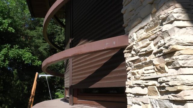 Raising shutters on a window in a modern house. Stone cladding on the facade and brown roller blinds. Green trees in the background.