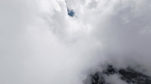 Aerial view flying through clouds above mountain terrain