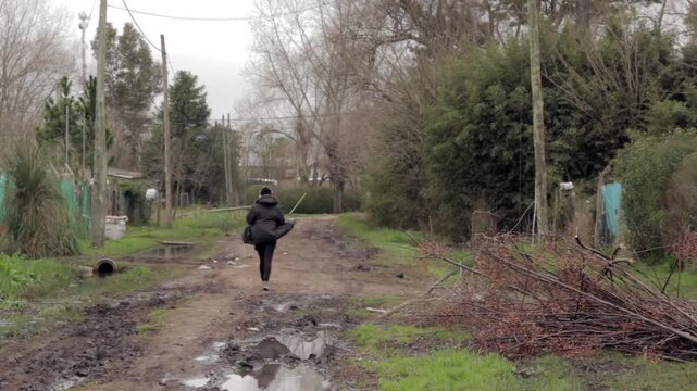 Woman Walking Away Down Muddy Dirt Road In Poor Suburban Neighborhood, Buenos Aires Province, Argentina