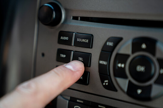 Finger pressing telephone button on automotive dashboard console for wireless handsfree connection.