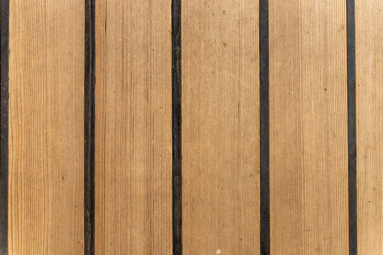 Vertical wooden teak deck planks with black caulked seams on a boat, macro background texture of maritime flooring.