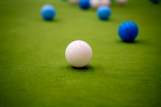 White plastic ball in focus on bright green carpet surface with blurred blue balls scattered in background.