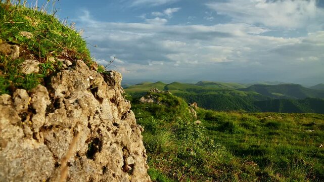 Rocky outcrop overlooking green hills and cloudy sky