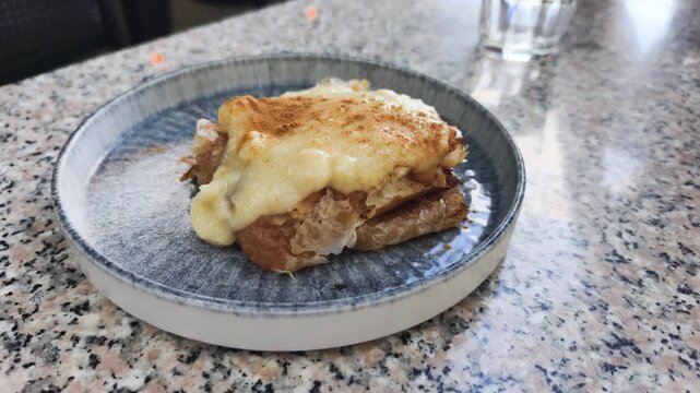 Traditional apple strudel with creamy vanilla sauce sits on ceramic plate. Warm apple strudel sprinkled with cinnamon powder serves as classic Austrian dessert for sweet lunch in local cafe.