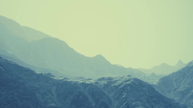 The scene shows layered mountains under a soft light during early morning. The landscape appears vast with gentle contours and minimal detail in the distance.