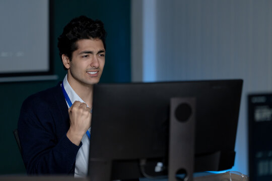 Adult male technology professional reacts with frustration at computer monitor in modern office, expressing work pressure during software troubleshooting, cybersecurity review, and system analysis.