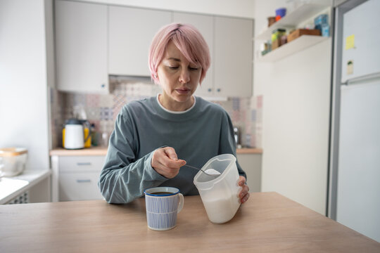 Mature woman adds spoonful of white sugar to to coffee at home, illustrating habitual sweetening, sugar dependence and difficulty reducing added sugar despite efforts to change unhealthy behavior.