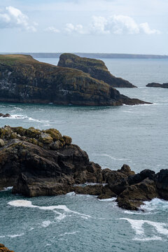 Haverfordwest, United Kingdom - 03 August 2024: View of Skomer Island featuring rugged coastal cliffs, rocky outcrops, and crashing waves under a cloudy sky.