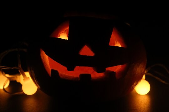 flat lay of a glowing halloween pumpkin in the dark with small lamps