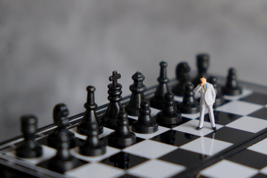 Miniature businessman standing on chessboard facing opponent pieces, business strategy, decision making, risk management, and leadership concept